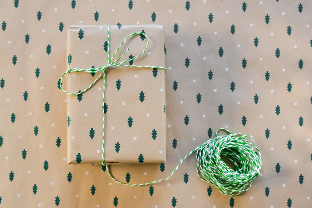 Tan wrapping paper with small pine trees and white dots background and gift wrapped with paper and green and white twine