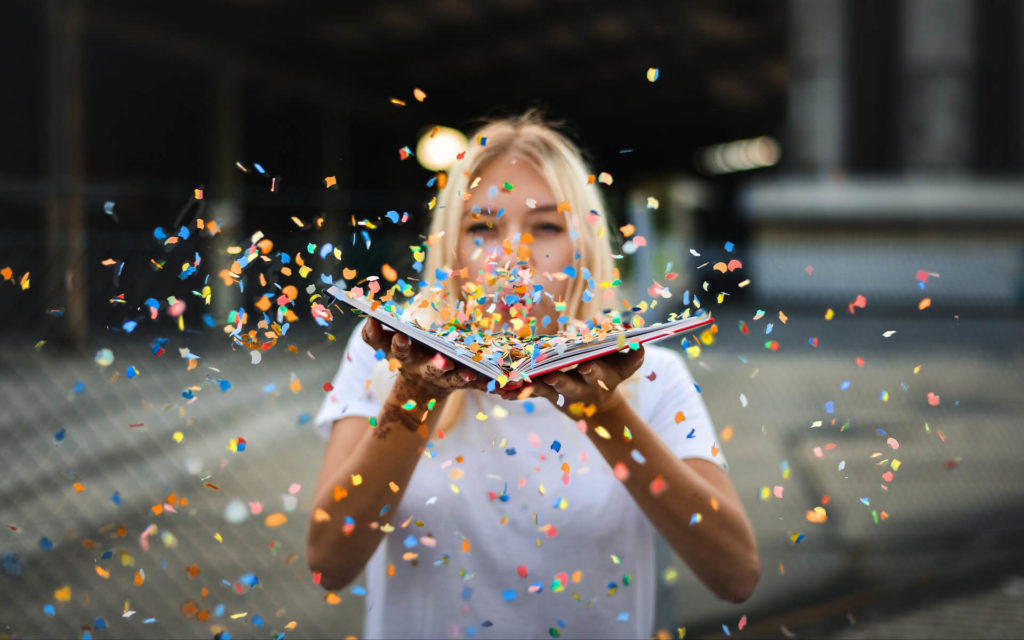 Blonde woman with an open book blowing colorful paper confetti from book pages outwards