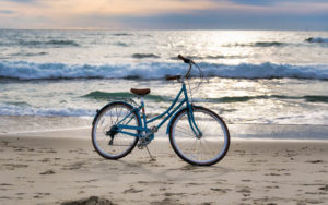 Aqua blue bicycle on beach with waves coming in and pinkish clouds