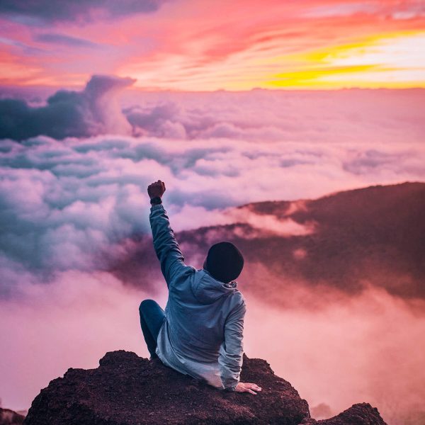 A man showing personal power atop a rock outcropping above the clouds. Show your power, have it all, prosperity, abundance, and joy. Explore a Mind Beliefs course!