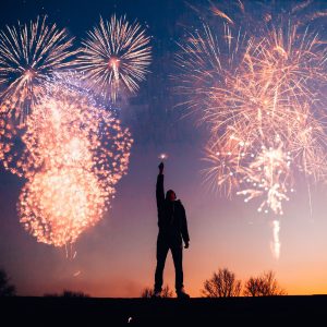 Man with an upraised hand with a firecracker and fireworks behind him. Expand your magic with a Mind Truths course!