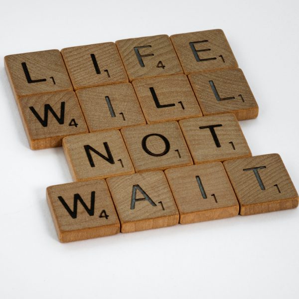 Word scrabble pieces spelling out "Life Will Not Wait." Learn to overcome procrastination with a Mind Truths course!
