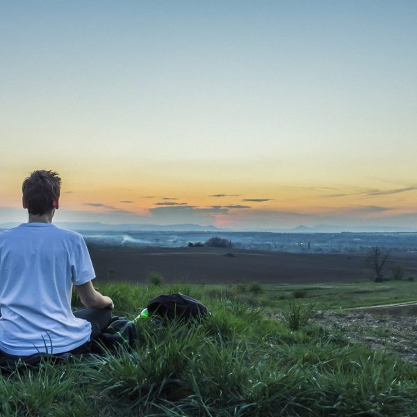 A man sitting in a meadow overlooking the ocean practicing meditation at sunset.