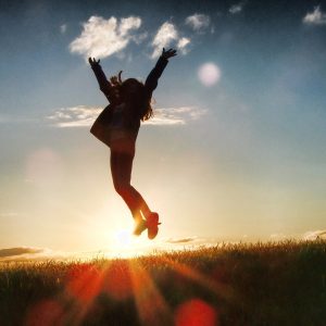 Woman jumping for joy in a sunlit field. Discover your undefeatable winning mindset with our Mind Truths course!